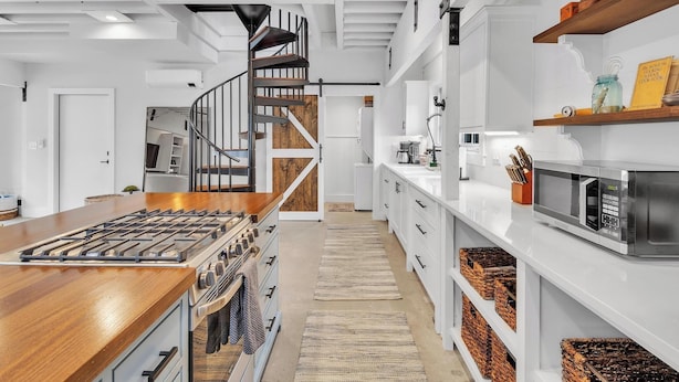 Una cucina moderna con isola centrale, elettrodomestici in acciaio inossidabile e una scala in legno che conduce a un piano superiore.