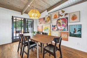 A dining area with a wooden table and chairs, surrounded by various artworks on the walls.