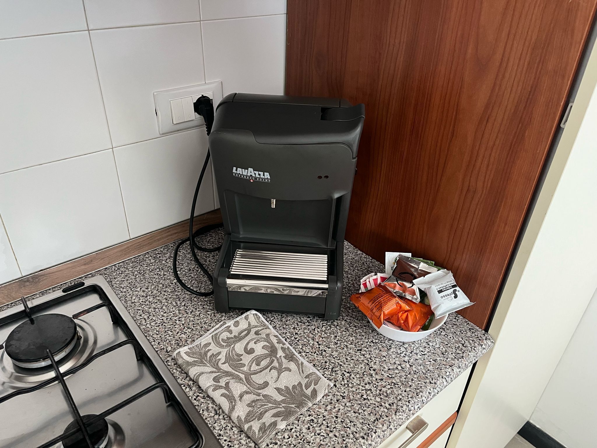 Una cocina con cafetera, estufa a gas y un paquete de cápsulas de café.