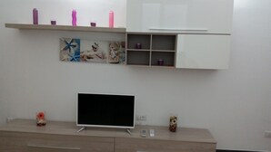 A modern living room with a flat-screen TV on a wooden cabinet, a white cabinet with shelves above, and a decorative wall piece. - Nice Apartment With sea View in Genoa (Genoa)