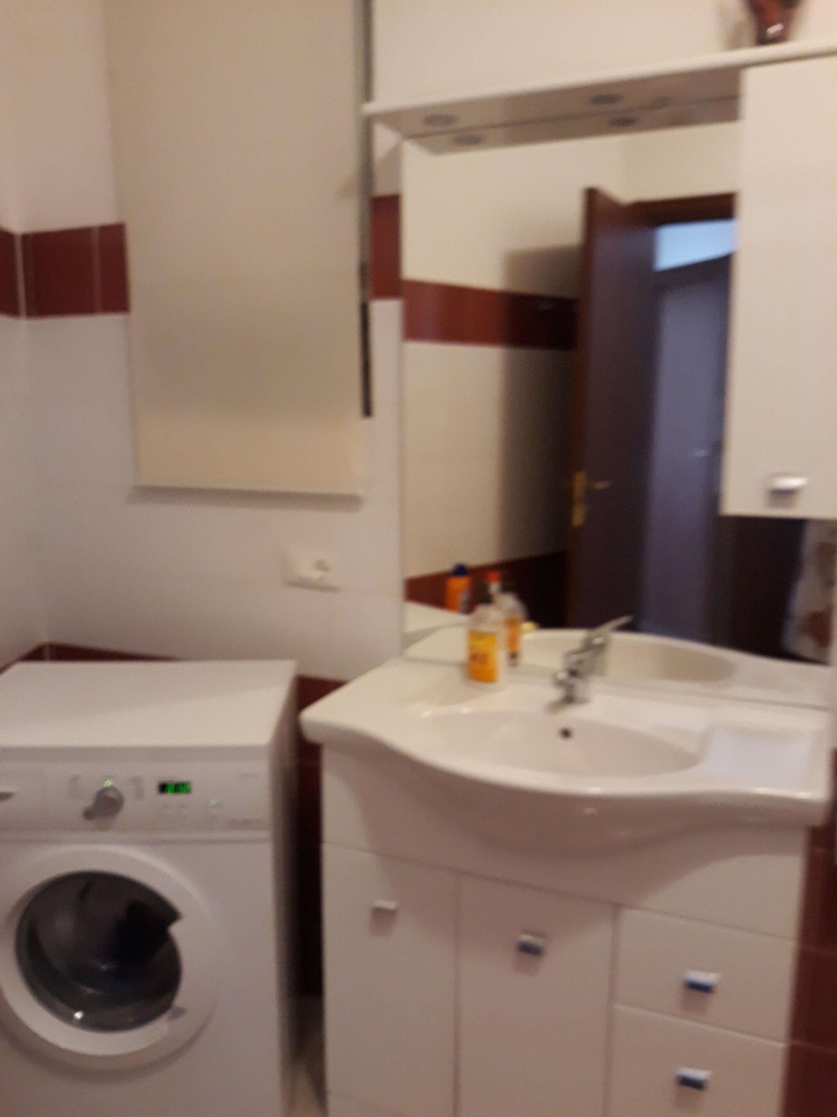 Ein kleines Badezimmer mit Waschmaschine, Waschbecken und Spiegel.
