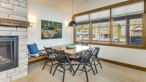 A dining area with a stone fireplace, a large window with blinds, and a colorful deer painting on the wall. - Mountain Views: Luxurious Grand Lake Escape! (Grand Lake)