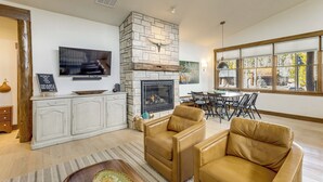 A living room with a stone fireplace, leather sofas, a dining area, and a large window. - Mountain Views: Luxurious Grand Lake Escape! (Grand Lake)