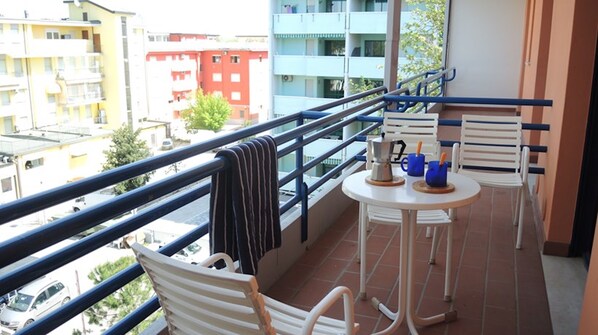 A balcony with white chairs and a small table, a metal railing, and a view of buildings in the background. - Stunning Apartment Near the Beach - Beahost (San Michele al Tagliamento)