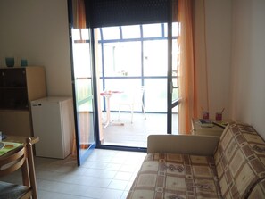 A compact living space with a kitchenette, a sofa, and a sliding glass door leading to an outdoor area with a table and chairs. - Stunning Apartment Near the Beach - Beahost (San Michele al Tagliamento)