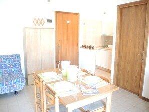 A dining area with a wooden table set for four, a blue patterned sofa, and a kitchen in the background. - Stunning Apartment Near the Beach - Beahost (San Michele al Tagliamento)