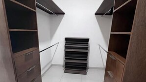 Un vestidor con estantes y cajones de madera, un perchero metálico y piso cubierto de baldosas blancas.