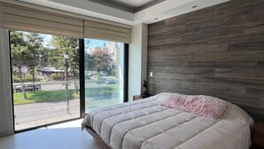 Un dormitorio moderno con una cama grande, vistas al exterior a través de un ventanal corredero y un cabecero de madera.