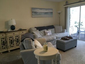 A living room with a striped sofa, a small round table with a candle, a lamp, and a view of the outdoors through a sliding door.