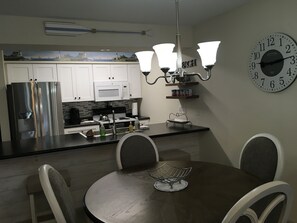 A modern kitchen with white cabinets, a stainless steel refrigerator, a microwave, and a dining area with a round table and chairs.