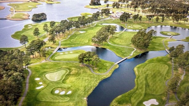Vista aérea de um campo de golfe com vários obstáculos de água, armadilhas de areia e uma ponte ligando diferentes áreas.