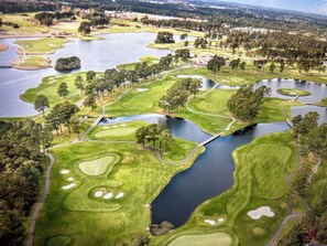 An aerial view of a golf course with multiple water hazards, sand bunkers, and a bridge connecting different areas.