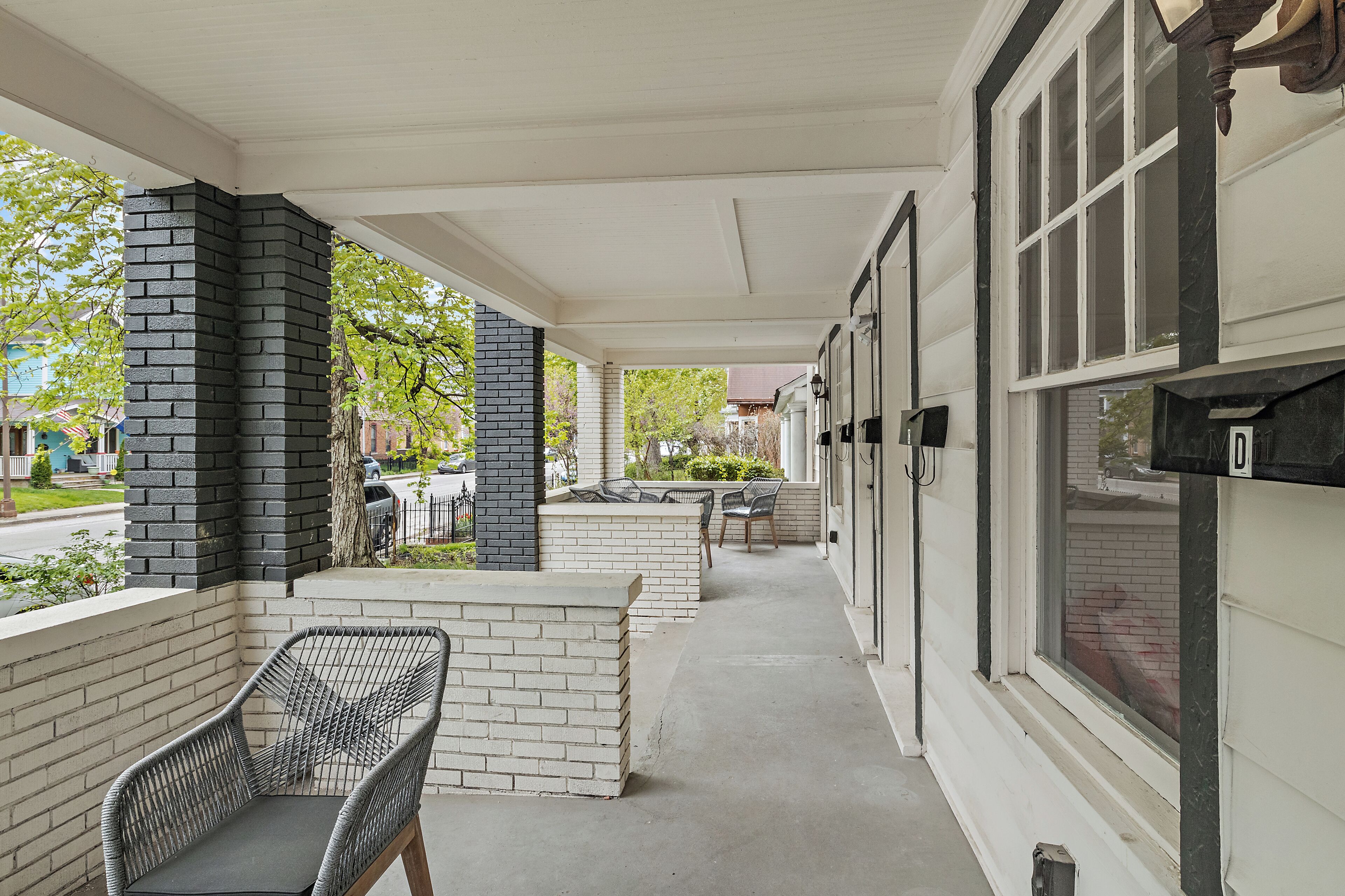 A covered porch with brick columns, outdoor seating, and a view of the street.