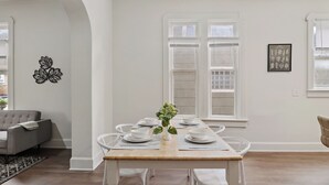 A dining area with a wooden table set for six, white chairs, a vase with a plant, and a wall-mounted decorative piece. - ⭐Modern 2 Bedroom Unit ⭐ Convenient ⭐ Near Downtown, Convention & Hospitals ⭐ (Indianapolis)