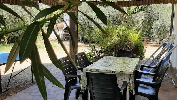 Un patio al aire libre con una mesa y sillas, rodeado de follaje y un edificio al fondo.