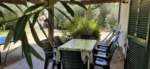 An outdoor patio with a table and chairs, surrounded by greenery and a building in the background.