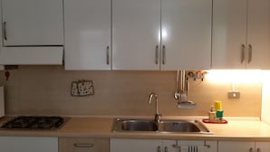 Cocina con armarios blancos, microondas, cocina a gas, lavaplatos y un ventanal pequeño.