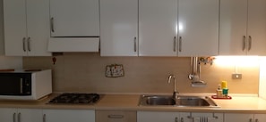 A kitchen with white cabinets, a microwave, a gas stove, a sink, and a small window. - Relax - Olive And Sea Sperlonga (Itri)