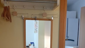 Una habitación con un espejo, una estantería blanca, una puerta de madera y suelo de baldosas.