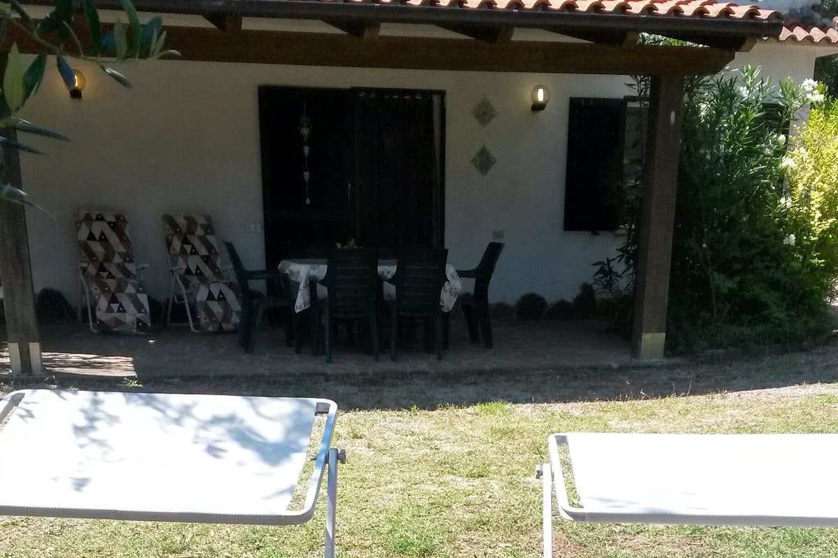 A patio area with metal chairs and a table, a building with a tiled roof, and some outdoor furniture.