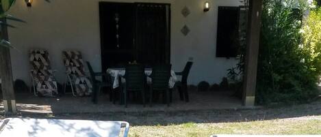 Un espacio de patio con sillas y una mesa de metal, un edificio con techo de tejas y algunos muebles de exterior.