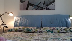 Un dormitorio con una cama, dos lámparas de noche, un cojín estampado y un cuadro abstracto colgado en la pared.