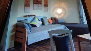 Ein kompakter Wohnraum mit einer Couch, einem kleinen Tisch und einem Stuhl. Über der Couch befinden sich drei an der Wand befestigte Kunstwerke.