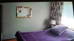 Ein Zimmer mit einem Bett, einem Wandspiegel, einer Lampe und einem Fenster mit Vorhängen.