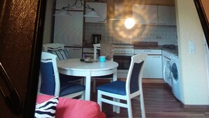 Eine kompakte Küche mit Herd, Backofen und Waschmaschine. Es gibt einen Esstisch mit Stühlen sowie eine Couch mit einem gemusterten Kissen.