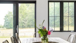 Un coin repas avec une table en bois, des chaises, un vase de fleurs et une vue dégagée grâce à de grandes fenêtres.