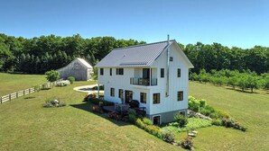 Une maison blanche à deux étages, dotée d’un balcon, entourée d’une pelouse bien entretenue et avec un vignoble en arrière-plan.