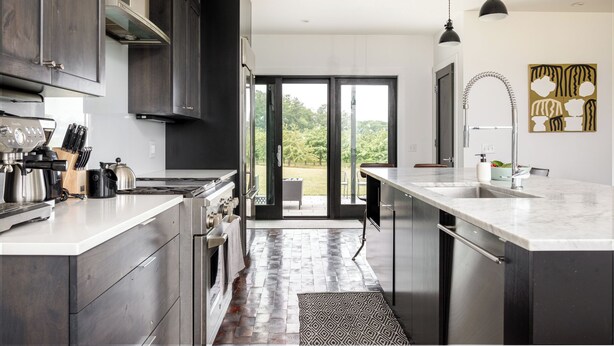 Une cuisine moderne avec des meubles de couleur sombre, un grand îlot central et une vue sur l’extérieur.