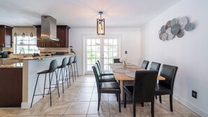 Una cocina moderna con una isla grande, taburetes de bar y un comedor con mesa y sillas de madera.