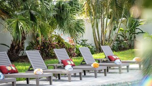 Un área junto a la piscina con sillones de descanso y toallas, rodeada de exuberante vegetación y palmeras.
