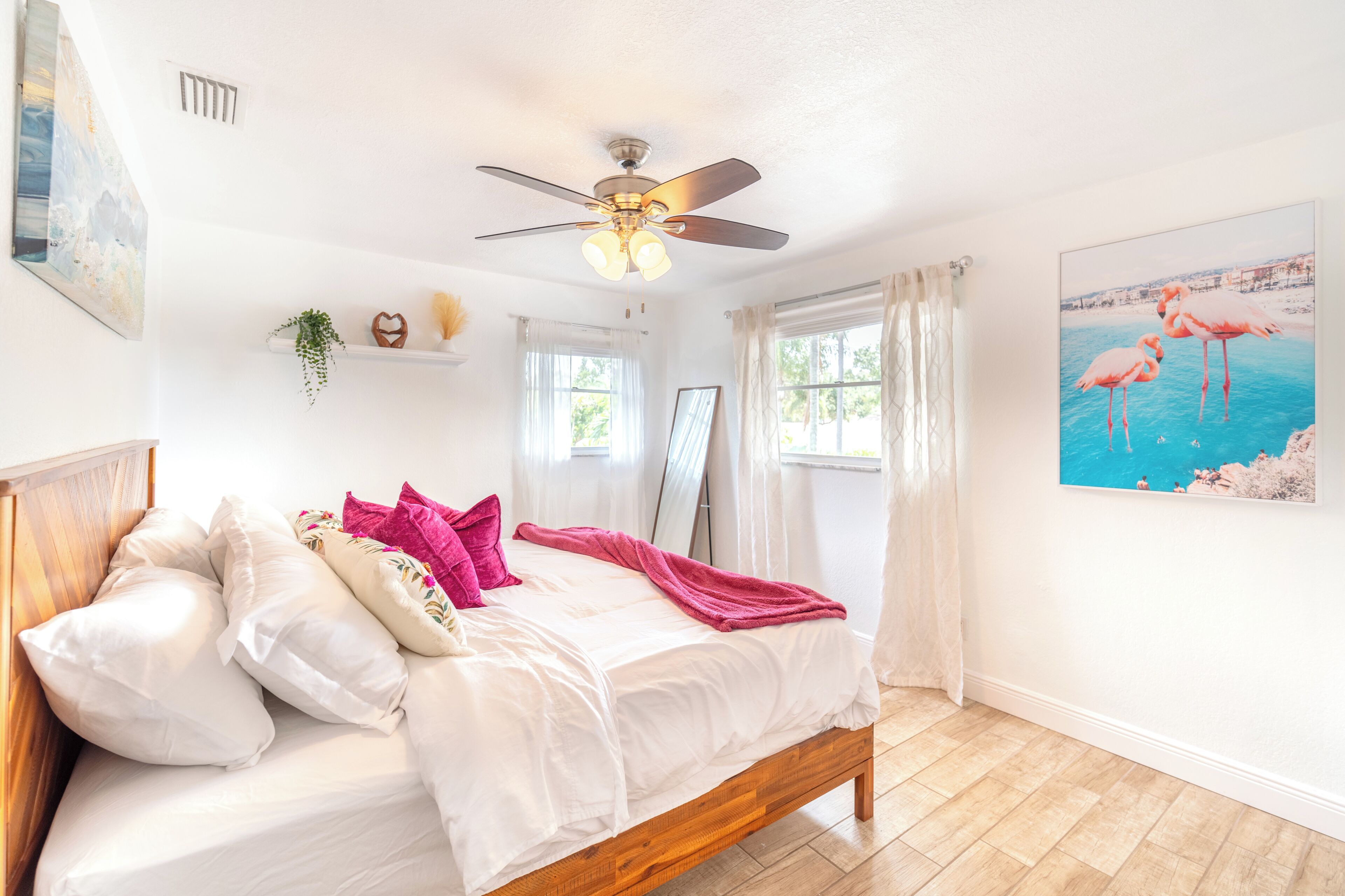 A bedroom with a bed, ceiling fan, white walls, and a window with curtains.