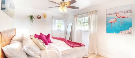 A bedroom with a bed, ceiling fan, white walls, and a window with curtains.