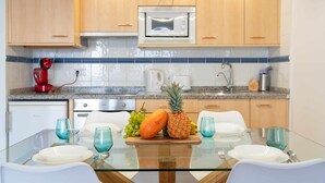 Una cocina moderna con armarios de madera, microondas y una mesa de comedor de cristal preparada para dos.