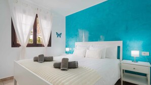 Un dormitorio con una cama grande, ropa de cama blanca, una pared de acento color verde azulado, una ventana con cortinas y una mesita de noche con una lámpara.