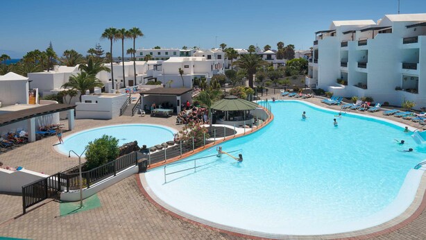 Una piscina rodeada de edificios blancos, palmeras y sillas de descanso.