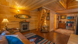 Ein gemütliches Blockhaus-Interieur mit Wohnzimmer, Kamin, Küche und einem Schlafzimmer im Obergeschoss.