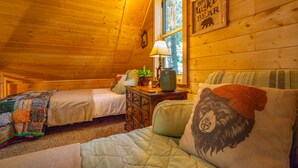 Une chambre confortable dans un chalet, avec deux lits, une lampe et un coussin à motifs d’ours.