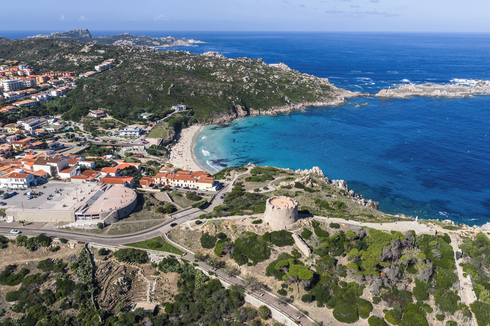 An aerial view of a coastal town with a beach, a castle, and surrounding greenery.
