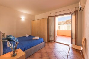 Ein Schlafzimmer mit Bett, Stuhl, Schreibtisch und einer Glastür, die zu einem Außenbereich führt.
