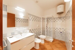 Ein Badezimmer mit großem Spiegel, Waschbecken in Weiß, Toilette und Duschbereich.