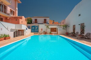 Ein Schwimmbecken mit Holzterrasse, umgeben von Gebäuden mit Balkonen und Blumentöpfen.