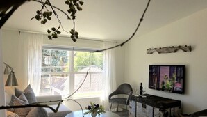 A modern living room with a sofa, a round table with a vase, a dark wooden cabinet, and a large window with curtains. - Urban Lifestyle, Lakes District of MPLS! Quiet Family Neighborhood, 1BR, 1BA (Minneapolis)