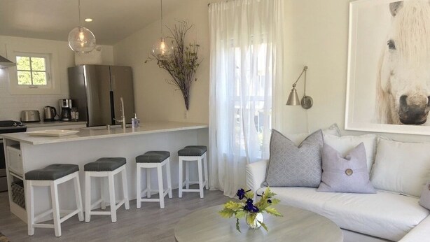A modern kitchen with a stainless steel refrigerator, a white dining area with bar stools, a round coffee table with flowers, and a white sofa with cushions. - Urban Lifestyle, Lakes District of MPLS! Quiet Family Neighborhood, 1BR, 1BA (Minneapolis)