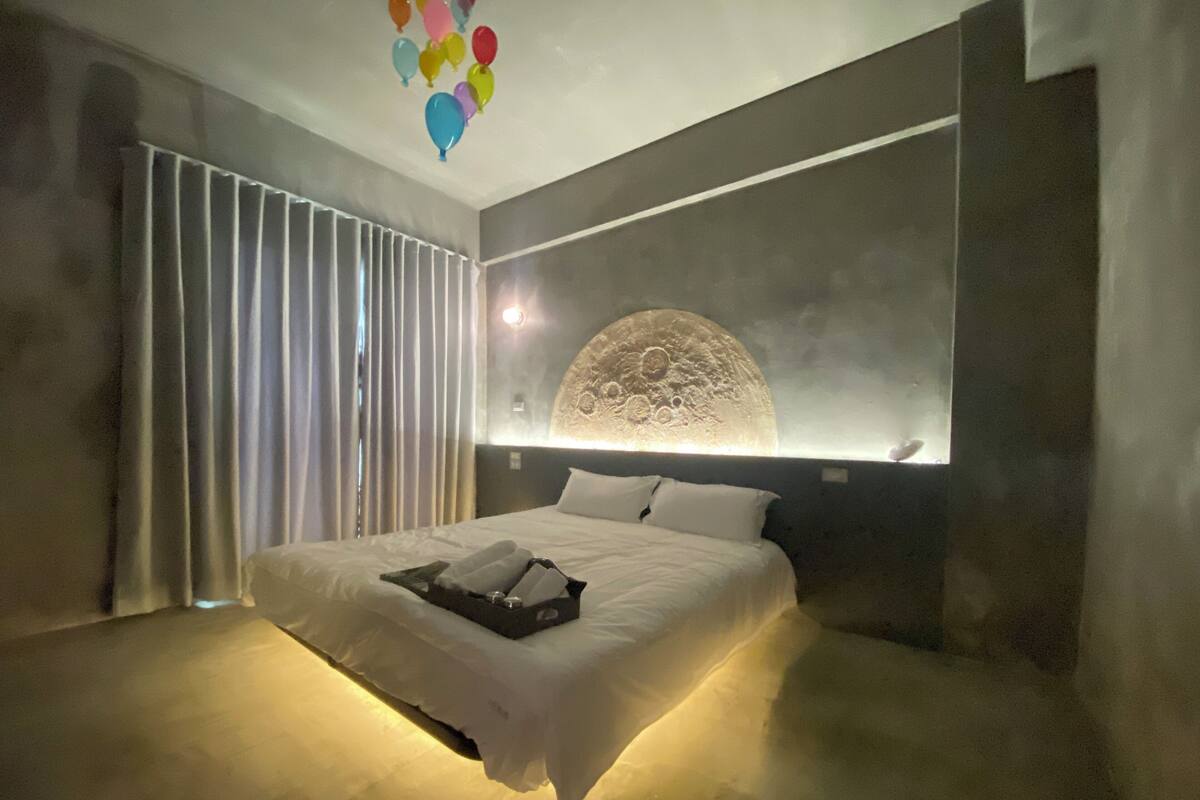 Una habitación de hotel moderna con una cama grande, un elemento decorativo en la pared que recuerda a la luna y vistas al cielo a través de cortinas.