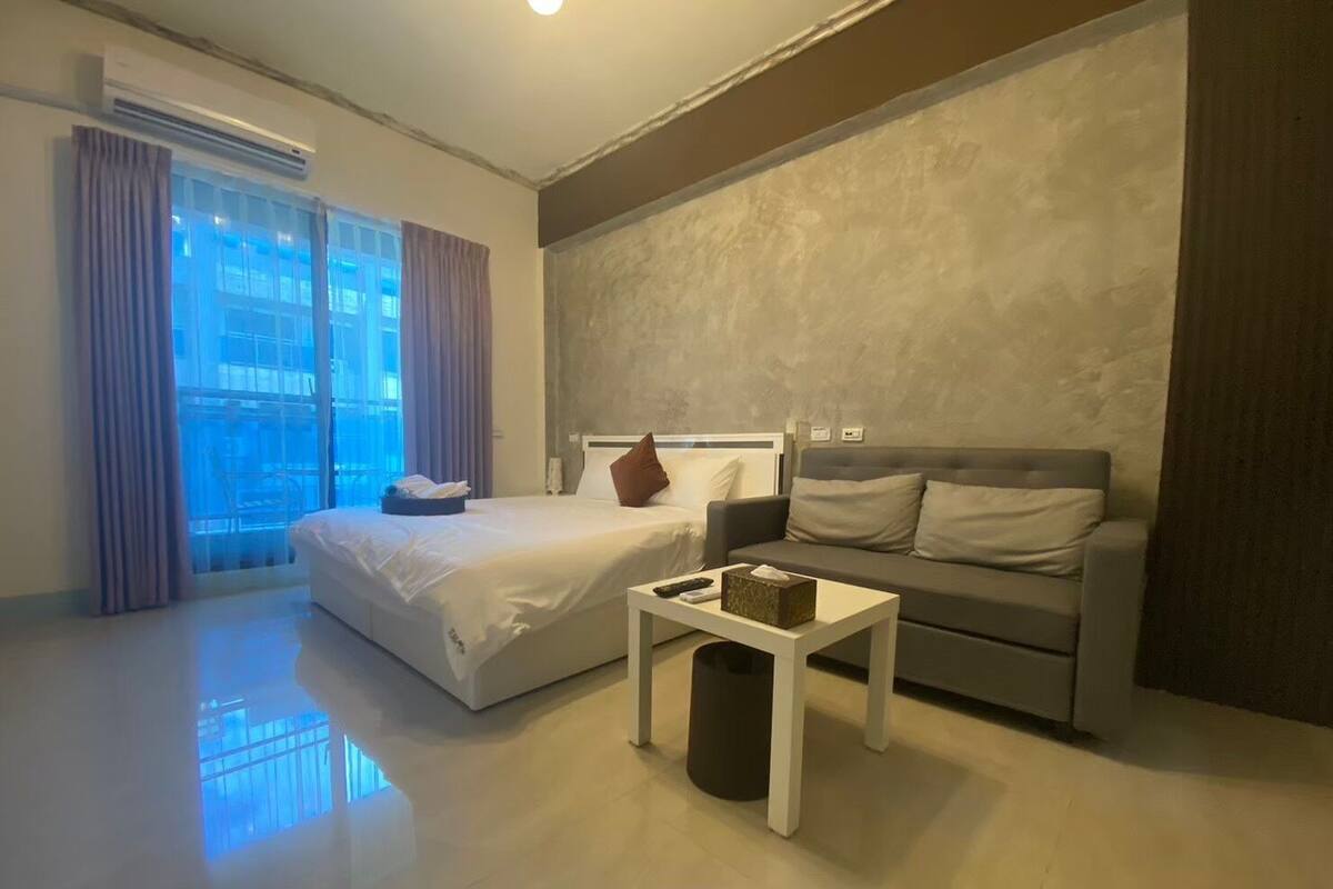 Una habitación de hotel moderna con una cama, un sofá, una mesita y un cubo de basura.