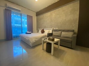 A modern hotel room with a bed, a sofa, a small table, and a trash bin. - Have fun B&B (Hengchun)